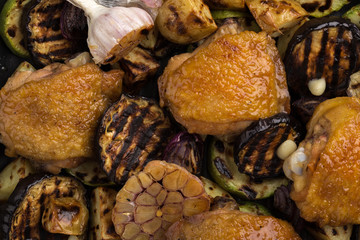 Chicken thighs with grilled vegetables. Chicken served in a frying pan on an old wooden table. Chicken with lime, zucchini, eggplants, onions and garlic. Close-up shot. Free space for text.