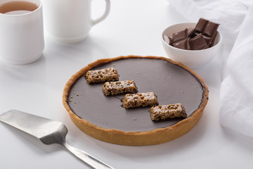 A cake with chocolate and nuts. Served on a white table with tea and a white napkin. Homemade cake on white background.