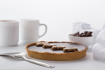 A cake with chocolate and nuts. Served on a white table with tea and a white napkin. Homemade cake on white background.