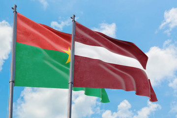 Latvia and Burkina Faso flags waving in the wind against white cloudy blue sky together. Diplomacy concept, international relations.