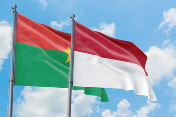 Fototapeta na wymiar Monaco and Burkina Faso flags waving in the wind against white cloudy blue sky together. Diplomacy concept, international relations.
