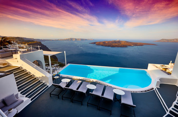 Fototapeta premium Swimming pool on the hotel terrace of fira's town on Santorini island, Greece. Incredibly romantic sunset on Santorini. Oia village in the morning light. Amazing sunset view with white houses.