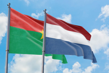 Netherlands and Burkina Faso flags waving in the wind against white cloudy blue sky together. Diplomacy concept, international relations.