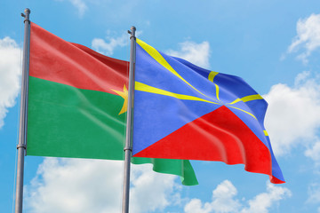 Reunion and Burkina Faso flags waving in the wind against white cloudy blue sky together. Diplomacy concept, international relations.