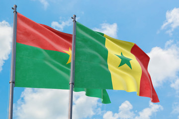 Senegal and Burkina Faso flags waving in the wind against white cloudy blue sky together. Diplomacy concept, international relations.