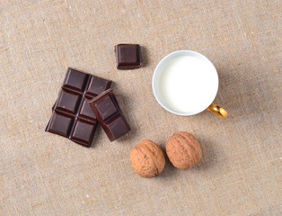 pieces of dark chocolate, walnuts, cup of milk on sackcloth