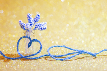 Blue thread in the shape of a symbol of love of heart and a vase of flowers on a gold background for Valentine's day