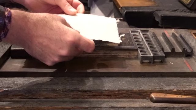 Hands placing paper on a printers block and pushing the block into a Gutenberg press
