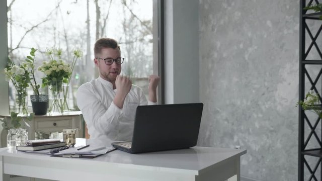 business success, a young male small business owner rejoices at good working position while sitting at table with laptop, male entrepreneur conducts business online