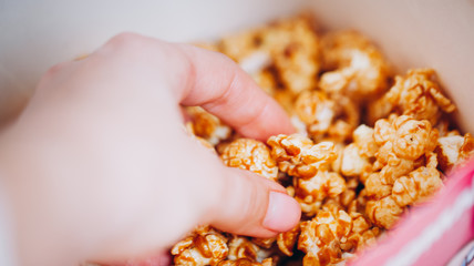 woman hand takes from a box of sweet popcorn  in a movie theater cinema rest entertainment