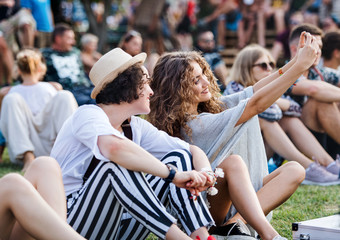 Fototapeta premium Group of young friends sitting on ground at summer festival.