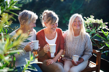 Senior women friends with coffee sitting outdoors on terrace, resting.