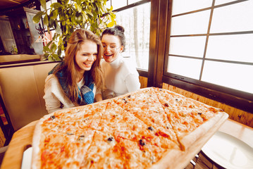Girls in a pizzeria with a huge sliced pizza. Big pizza on the table. Girlfriends in a cafe