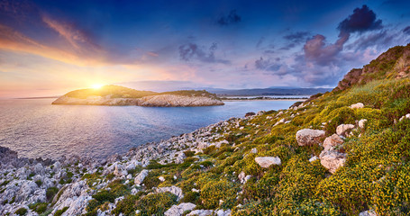 Amazing sunset view with multicolored clouds. Incredibly sunrise on Voidokilia beach, Ionian Sea, Pilos town, Greece, Europe. View of the ocean through the rocky shore