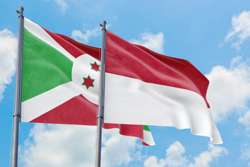 Monaco and Burundi flags waving in the wind against white cloudy blue sky together. Diplomacy concept, international relations.