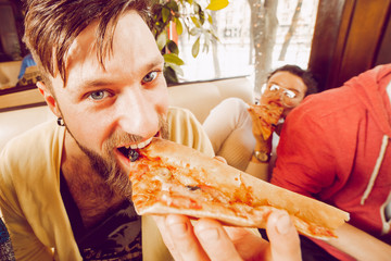 A young guy with a beard bites a large piece of pizza closeup. Friends party at the pub. Close-up portrait