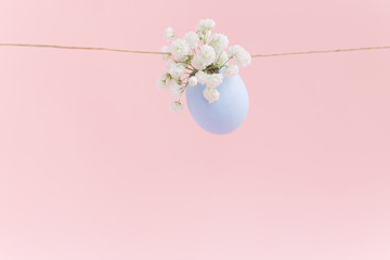 Easter blue flying eggshell with gypsophila white flowers, hanging on a rope on light pink background. Egg is symbol of celebration of religious holiday among Catholics, Christians and Protestants
