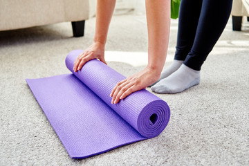 Close up image of woman rolling purple fitness or yoga mat after sport practice, pilates or working out at home or in studio, copy space