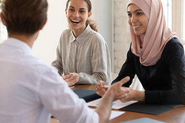 Happy multiracial employees laugh discussing ideas at meeting