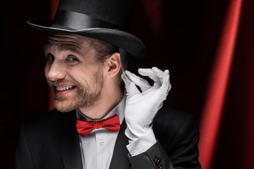 smiling magician holding playing card in circus with red curtains