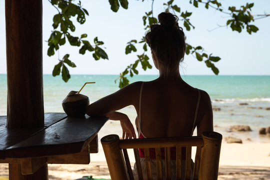 Young and sexy woman sitting in authentic beach bar with a coconut drink