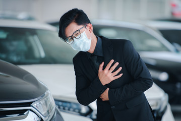 A handsome Asian businessman is in a car sales office and he is sick and he wears a mask while working on business concepts.- Colona virus