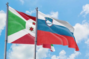 Slovenia and Burundi flags waving in the wind against white cloudy blue sky together. Diplomacy concept, international relations.