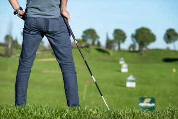 golf player with cap leaning on a golf club looking at the course
