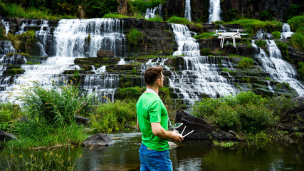 Traveler man controlling drone near the big Da lat waterfall. Drone pilot in beautiful landscape of Pongour waterfall.