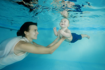 Mom with a little son dives underwater in a swimming pool