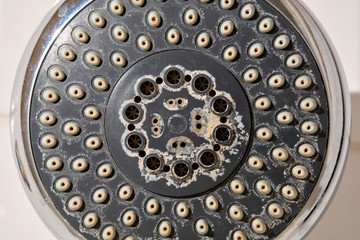 Close-up of an old used silver and grey colored shower head with limescales in the bathroom in front of white tiles