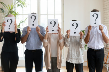 Diverse employees hide faces holding sheets with question marks