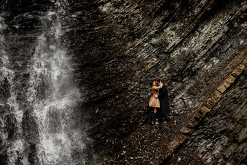 beautiful waterfall in the rock, a young couple of travelers walk on a rocky terrain. Stylish man wearing a hat