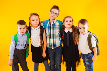 Smart schoolchildren smiling and looking at camera over yellow background. Happy kids in school uniform with backpacks