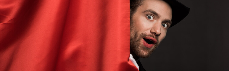 panoramic shot of shocked handsome magician in suit and hat in circus with red curtains © LIGHTFIELD STUDIOS