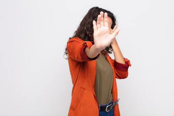 young pretty woman covering face with hand and putting other hand up front to stop camera, refusing...