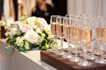 Many wine glasses with rose and white champagne stand in row on wooden desk on the clothing store presentation