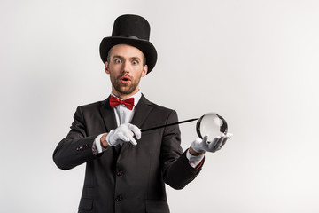 surprised magician holding wand and magic ball, isolated on grey