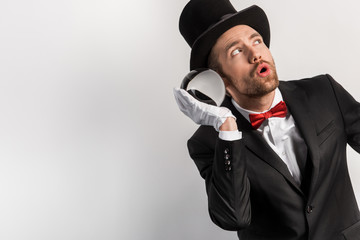shocked magician listening to magic ball, isolated on grey