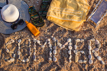 Fototapeta na wymiar Top view of the sandy beach by the sea, beach items are laid out on the sand. The word SUMMER is laid out of stone