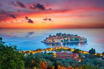 Amaizing sunset view on Sveti Stefan Island City. Small islet and resort in Montenegro. Balkans, Adriatic sea, Europe. Dramatic red sky under a Saint Stefan peninsula. - obrazy, fototapety, plakaty