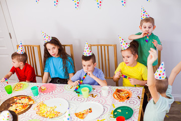 Kids celebrating a birthday with a pizza at cafe. Birthday party. Cute children in birthday hats having fun together