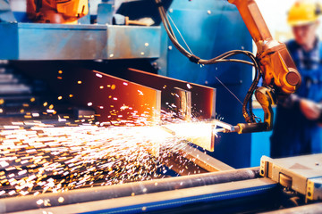 Worker controls robotic arm to cut steel in a factory.