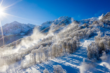 Fototapeta na wymiar Winter Mountain landscape at the Rosa Khutor ski resort in Sochi, Russia. Trees in hoarfrost against a beautiful morning sky in a frosty morning. Snow cannons sprinkle snow on the slopes
