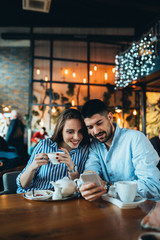 couple in cafeteria drinking tea and using mobile phone