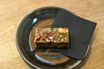 A delicious brown cake with nuts on a black plate with a black napkin on the table