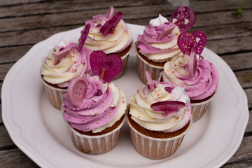 Birthday cupcakes on a ceramic plate in a rustic style. Vintage wooden background. Tasty cakes decorated with white and pink cream, candies and chocolate.Top view.