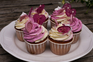 Birthday cupcakes on a vintage plate in a rustic style. Tasty cakes on old wooden background. Cupcakes decorated with white and pink cream, candies and chocolate.