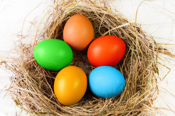Five Easter eggs painted with multi-colored paints lie in the shape of a flower in a nest of dry grass on a white background close-up.