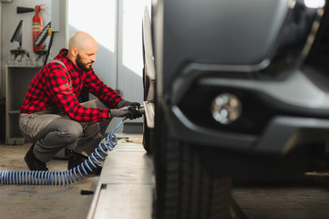 Mechanic changing a car tire in a workshop on a vehicle on a hoist using an electric drill to...